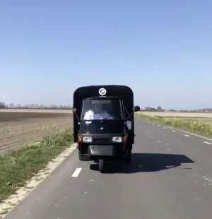 De tuk tuk ijskar van De IJsmobiel rijdt op een weg onderweg naar een evenement of feest